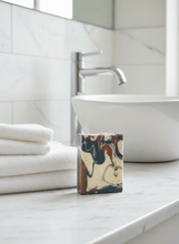 Load image into Gallery viewer, Bergamot & Sandalwood goat milk soap on a marble countertop next to white towels in a modern bathroom.