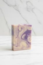 Load image into Gallery viewer, A rectangular bar of handmade soap with purple and cream swirls, standing on a gray slatted outdoor patio table.