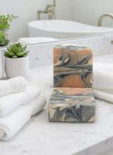 Load image into Gallery viewer, Guava Tea Goat Milk Soap bar with swirls of colors on a bathroom counter next to towels and a plant.
