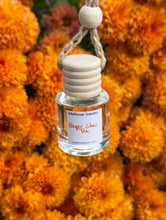 Load image into Gallery viewer, Ginger Chai Tea Car Diffuser hanging against a backdrop of vibrant orange flowers.
