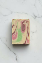Load image into Gallery viewer, A rectangular handmade soap bar with a marbled swirl pattern of cream, pink, green, and brown, resting on a white marble surface.