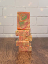 Load image into Gallery viewer, Colorful stacked bars of Tallow Soap with swirls of orange, pink, and green on a wooden surface.