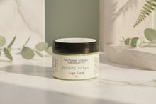 Load image into Gallery viewer, Jar of Woodland Whisper Exfoliating Sugar Scrub from Wildflower Soapary on a textured surface with a gray background.
