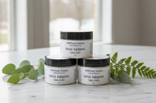 Load image into Gallery viewer, Three jars of Herbal Indulgence Tallow Butter surrounded by greenery on a marble surface.

