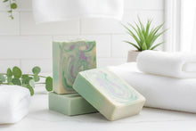 Load image into Gallery viewer, Tallow Goat Milk Soap - Rosemary bars with a creamy swirl design next to white towels and green foliage.
