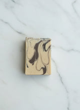 Load image into Gallery viewer, A rectangular bar of soap with a beige base and dark brown marbled swirls, placed on a white marble surface with gray veining.
