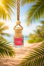 Load image into Gallery viewer, Coconut Colada hanging car diffuser surrounded by palm leaves evoking tropical vacation vibes.
