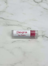 Load image into Gallery viewer, Sangria Lip Balm in a clear tube on a marble surface, perfect for hydration and fruity flavor.
