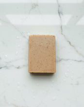 Load image into Gallery viewer, A rectangular bar of light brown soap with small dark specks, placed on a white marble surface with water droplets.
