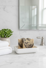 Load image into Gallery viewer, Two rectangular handmade soap bars with a marbled cream, beige, and dark brown swirl pattern, resting on a dark gray slatted wooden surface.
